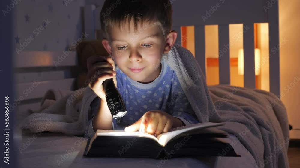 Little boy in pajamas lying in bed and reading bedtime story book with torch. Children education, development, secrecy, privacy, reading books Little boy in pajamas lying in bed and reading bedtime story book with torch. Children education, development, secrecy, privacy, reading books