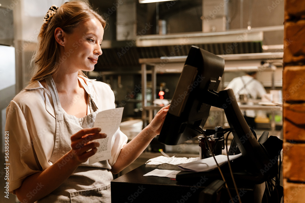 © Drobot Dean - Young woman holding order receipts while working in restaurant kitchen