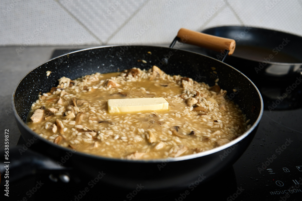 Process of cooking risotto. Arborio rice and piece of butter in frying pan in home kitchen. Italian cuisine dish
