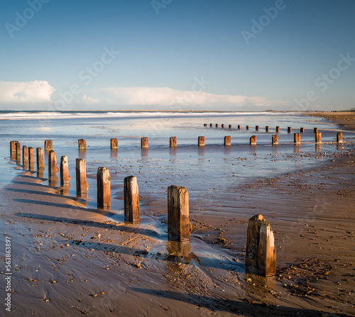 A row of wooden sea groynes in a zig zag formation on Brancaster beach, Norfolk photo