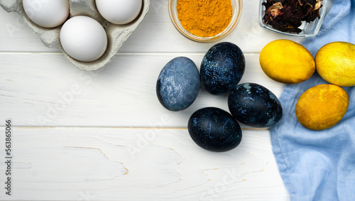 Easter composition with painted blue and yellow Easter eggs and natural food coloring on a wooden background. Banner. Top view. Copy space.