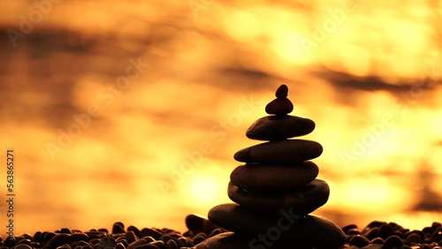 Balanced rock pyramid on pebbles beach. Golden sea bokeh on background. Selective focus  zen stones on sea beach  meditation  spa  harmony  calm  balance concept.