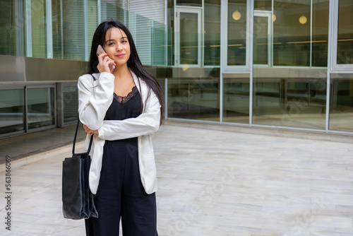 Close up portrait of a young executive businesswoman in urban outdoors calling with a smartphone. Smiling empowered woman dressed smart casual outside the office work site. Horizontal with copy space.