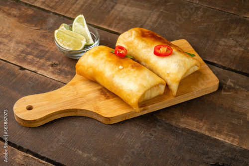 Mexican chimichanga with chili pepper on a wooden board, Mexican fast food.