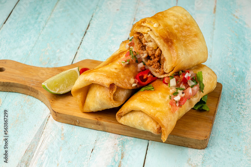 Chimichanga is a traditional Mexican fast food on a wooden board, one cut inside minced meat and beans. photo