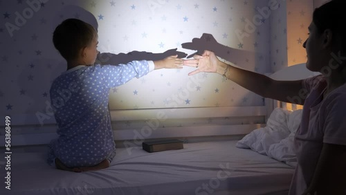 Cute boy with mother in pajamas playing with shadows on wall from hte flashlight. Family having time together, parenting, happy childhood and entertainment photo