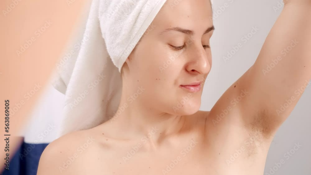 Happy smiling woman in bath towel looking on her hair growing under arms. Concept of beautiful female, natural beauty, feminity and body hair Happy smiling woman in bath towel looking on her hair growing under arms. Concept of beautiful female, natural beauty, feminity and body hair