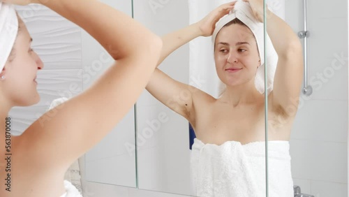 Smiling woman in bath towel lifting up arms and showing long dark armpit hair. Concept of hygiene, natural beauty, feminity and body hair growth
