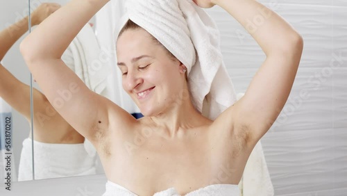 Young woman showing her under arm hair in bathroom. Concept of hygiene, natural beauty, feminity and body hair growth