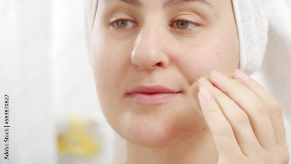 Closeup of young woman in bath towel applying cosmetics on face with soft sponge. Concept of beautiful female, makeup at home, skin care and domestic beauty industry. Closeup of young woman in bath towel applying cosmetics on face with soft sponge. Concept of beautiful female, makeup at home, skin care and domestic beauty industry.