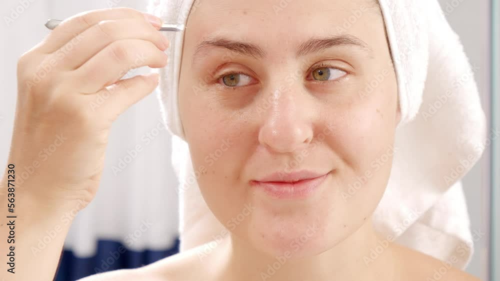 Young woman tweezing eyebrows after having shower in the morning. Concept of beautiful female, makeup at home, skin care and domestic beauty industry Young woman tweezing eyebrows after having shower in the morning. Concept of beautiful female, makeup at home, skin care and domestic beauty industry