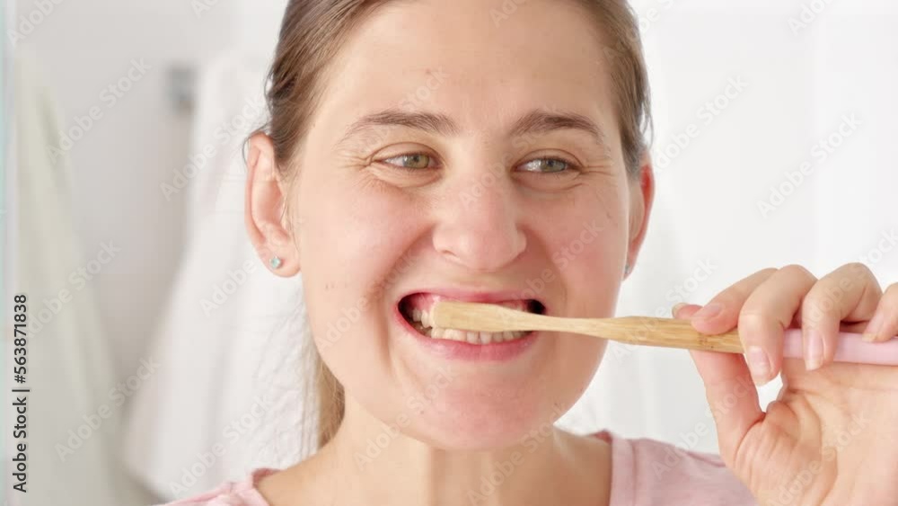 Slow motion shot of young woman brushing her teeth and looking in mirror. Concept of teeth health, self checking mouth and oral hygiene Slow motion shot of young woman brushing her teeth and looking in mirror. Concept of teeth health, self checking mouth and oral hygiene