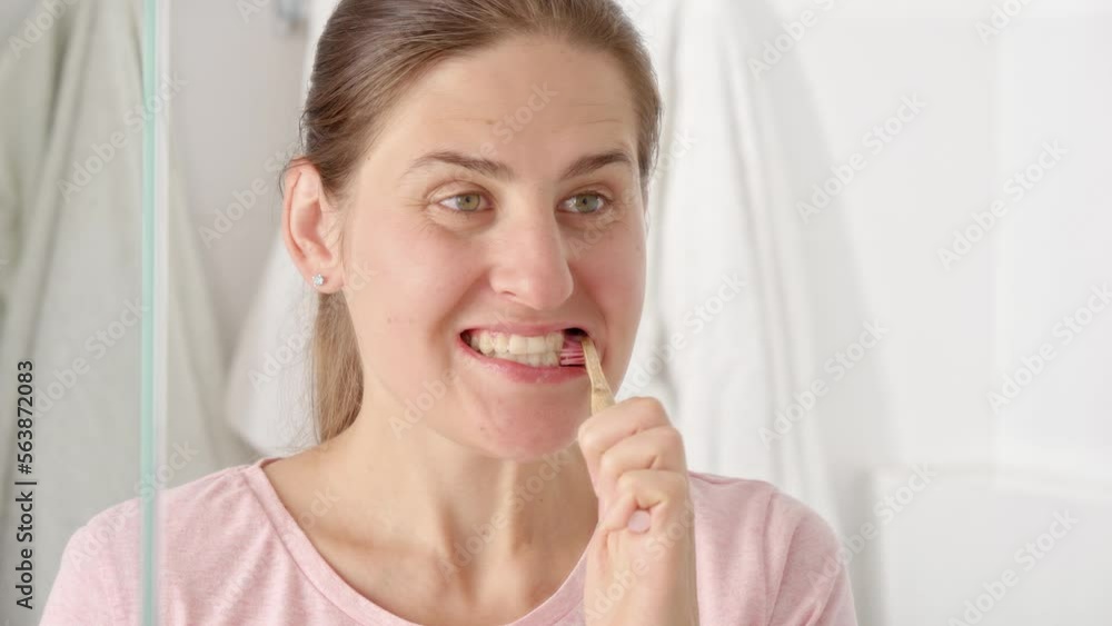 Portrait of young woman using wooden toothbrush and toothpaste to clean her teeth. Concept of teeth health, self checking mouth and oral hygiene Portrait of young woman using wooden toothbrush and toothpaste to clean her teeth. Concept of teeth health, self checking mouth and oral hygiene