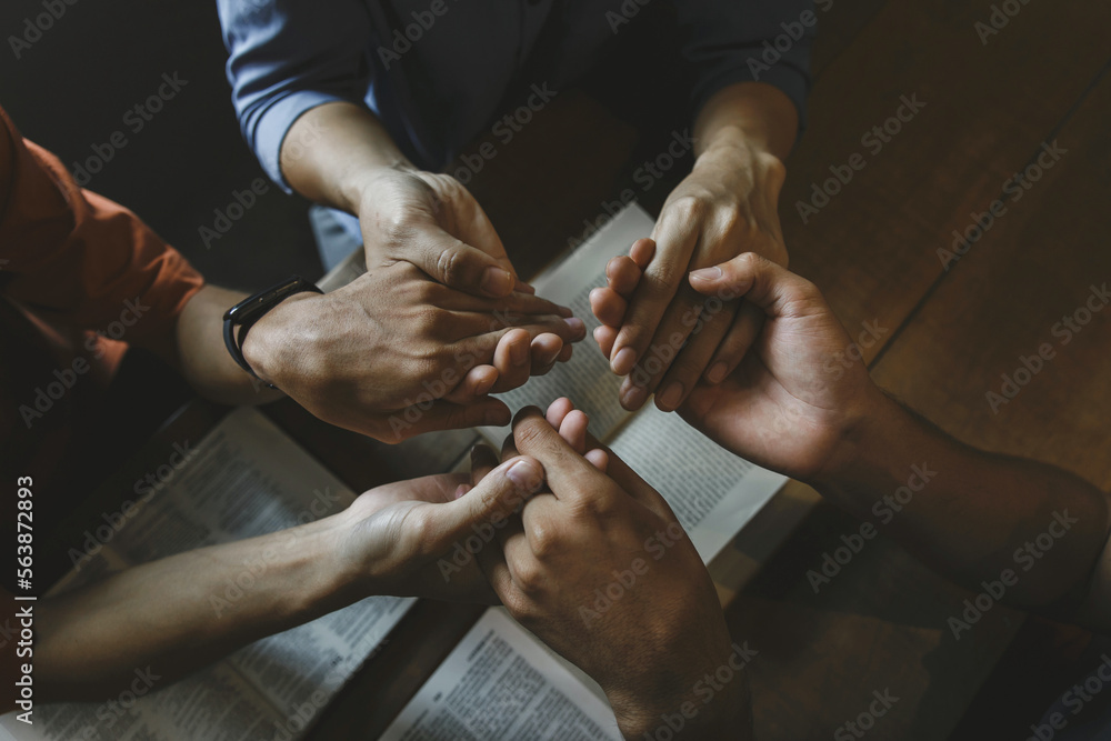Group of people holding hands praying worship believe with bible on a wooden table for devotional for prayer meeting. Christians and Bible study concept.believe in goodness.