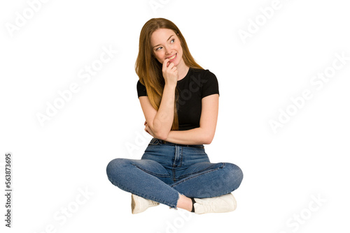 Young redhead woman sitting on the floor cut out isolated relaxed thinking about something looking at a copy space.