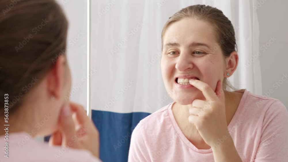 Beautiful smiling woman looking at her reflection in mirror and rubbing off the tooth plaque. Concept of teeth health, self checking mouth and oral hygiene Beautiful smiling woman looking at her reflection in mirror and rubbing off the tooth plaque. Concept of teeth health, self checking mouth and oral hygiene