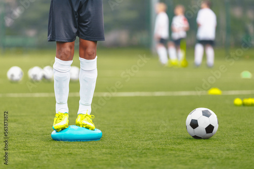 Soccer Player Standing on Stability Cushion on Grass Field and Improving Body Balance. Football Player Improving Skills With Personal Trainer. Football Equipment for Youth Players