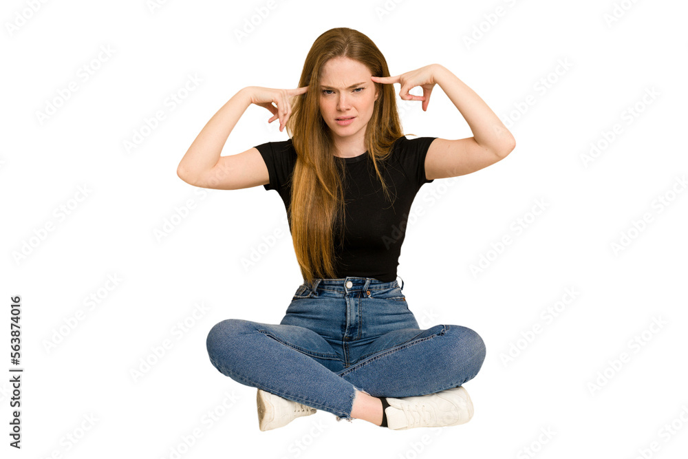 Young redhead woman sitting on the floor cut out isolated focused on a task, keeping forefingers pointing head. Young redhead woman sitting on the floor cut out isolated focused on a task, keeping forefingers pointing head.