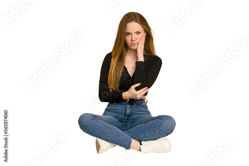Young redhead woman sitting on the floor cut out isolated smiling and showing a heart shape with hands.