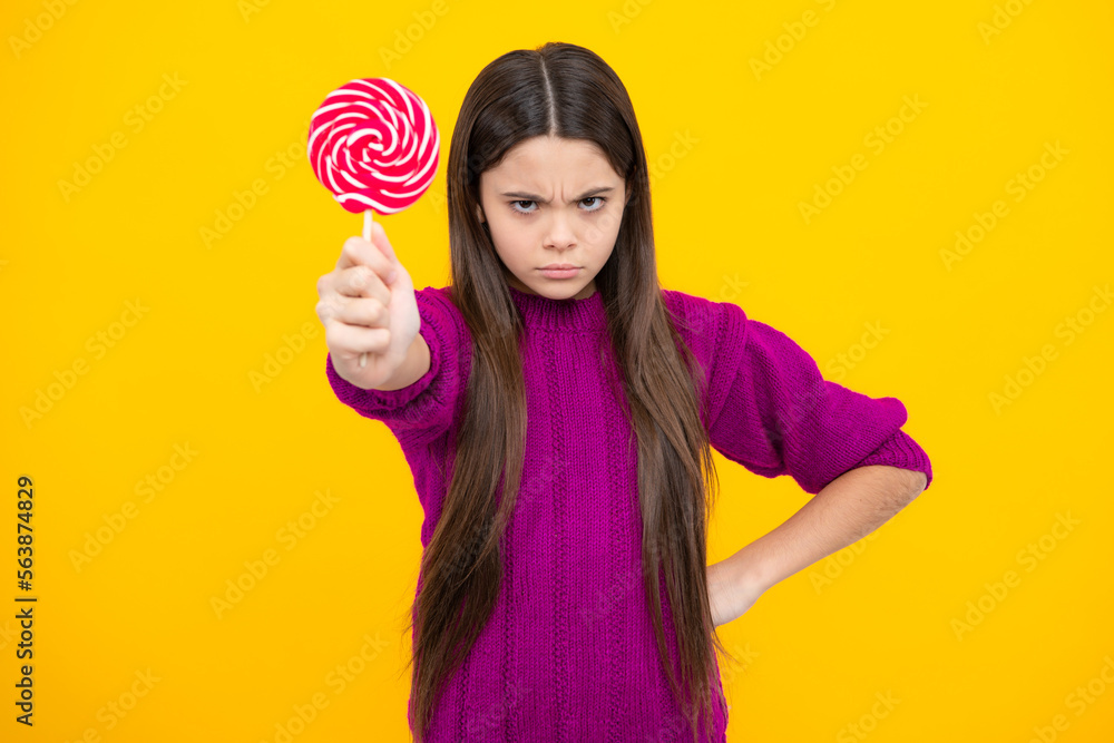 Teenager girl eating sugar lollypop. Candy and sweets for kids. Child eat lollipop popsicle over yellow isolated background. Yummy caramel, candy shop. Angry teenager girl, upset and unhappy.