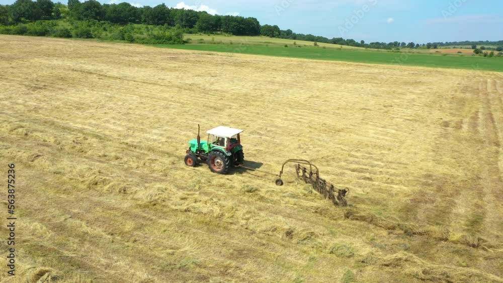 A tractor collects hay from the agricultural field. Farm machinery performs seasonal summer work on the field. Modern agriculture at drone view. 4K A tractor collects hay from the agricultural field. Farm machinery performs seasonal summer work on the field. Modern agriculture at drone view. 4K
