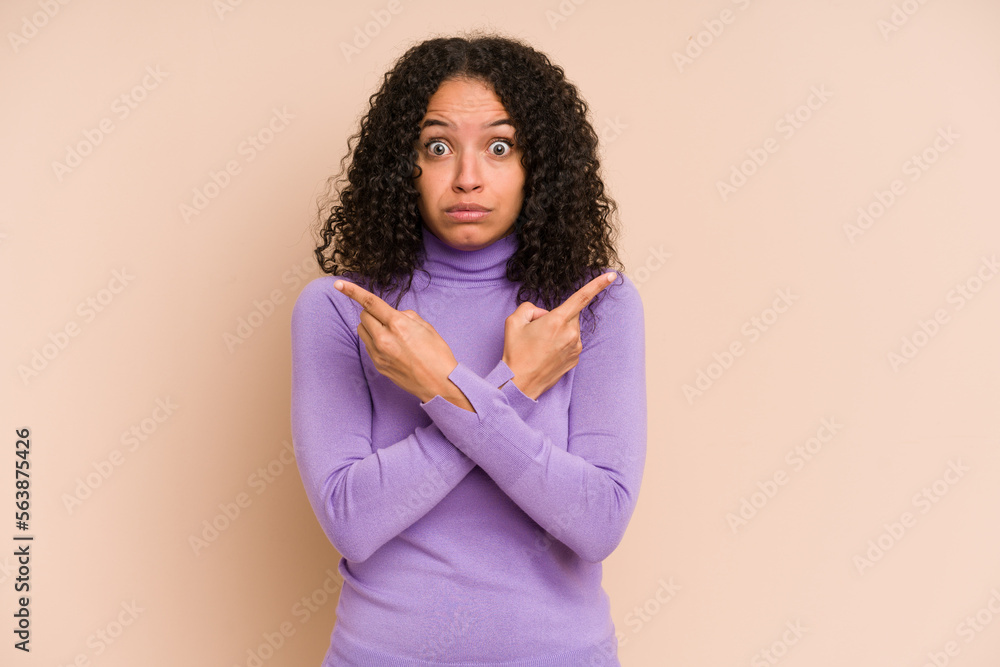 Young african american curly woman isolated points sideways, is trying to choose between two options. Young african american curly woman isolated points sideways, is trying to choose between two options.