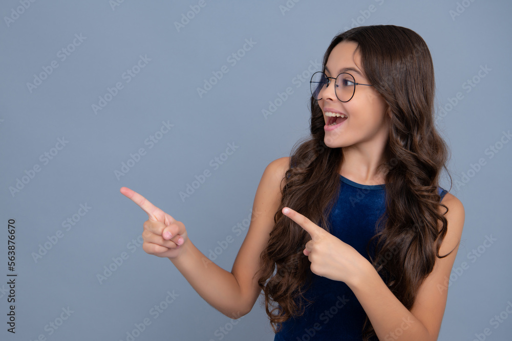 Obraz premium Wow, it's unbelievable. Shocked teenager child pointing aside at copy space. Teen girl pointing with two hands and fingers to the side. Happy girl face, positive and smiling emotions.