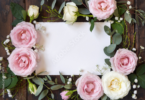 Horizontal card between pink and cream roses on brown wood top view, wedding mockup
