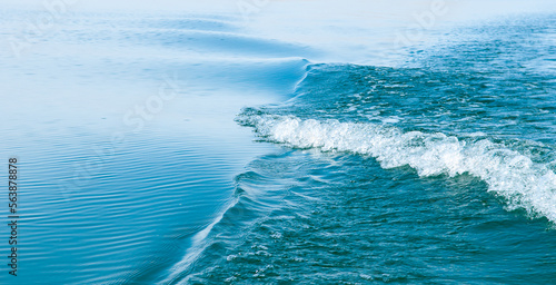 Waves on the sea. Water background, blue sea water. Beautiful texture of sun glare on water and sea foam. Waves from the ship.