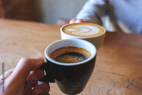 Closeup image of a couple people clinking coffee cups together in cafe