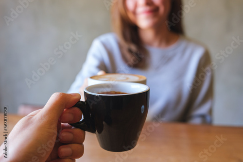 Closeup image of a couple people clinking coffee cups together in cafe
