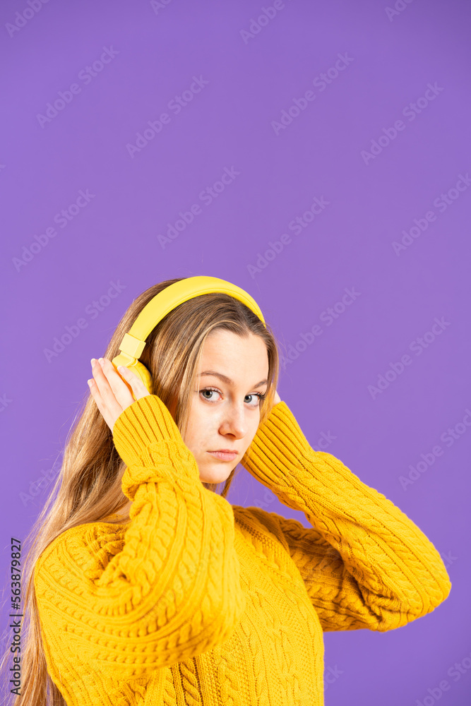 Portrait of young beautiful woman listening to music on headphones isolated on purple background with copy space