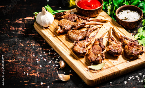 Grilled rack of lamb on a cutting board with parsley and tomato sauce. 