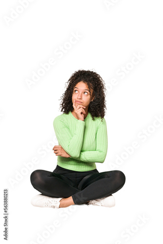 Young african american curly woman sitting on the floor isolated