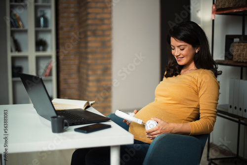 Smiling woman with headphones on her belly at work. Businesswoman in office.
