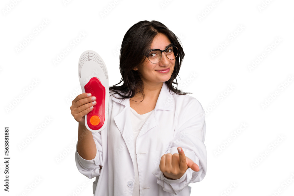 Young indian chiropodist woman holding a insoles for shoes cut out isolated pointing with finger at you as if inviting come closer.