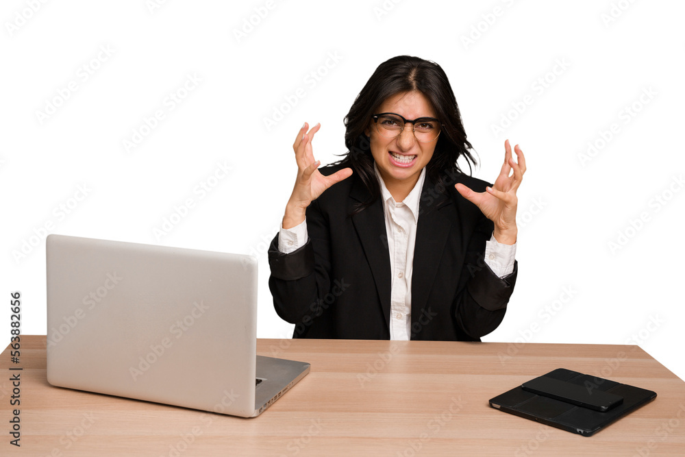 Young indian woman in a table with a laptop and tablet isolated screaming with rage. Young indian woman in a table with a laptop and tablet isolated screaming with rage.