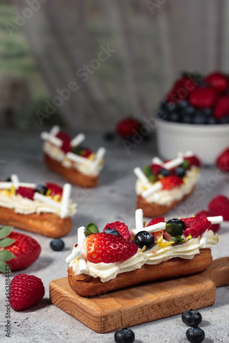 Freshly prepared éclairs topped with a medley of berries offer a tempting treat, blending the crispness of fruit with the softness of cream