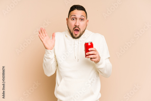 Young latin man holding a cola refreshment isolated surprised and shocked. © Asier