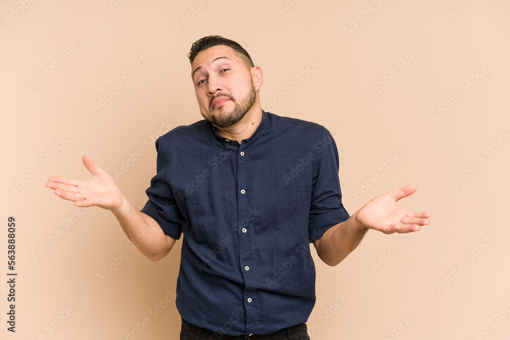 Adult latin man cut out isolated doubting and shrugging shoulders in questioning gesture.