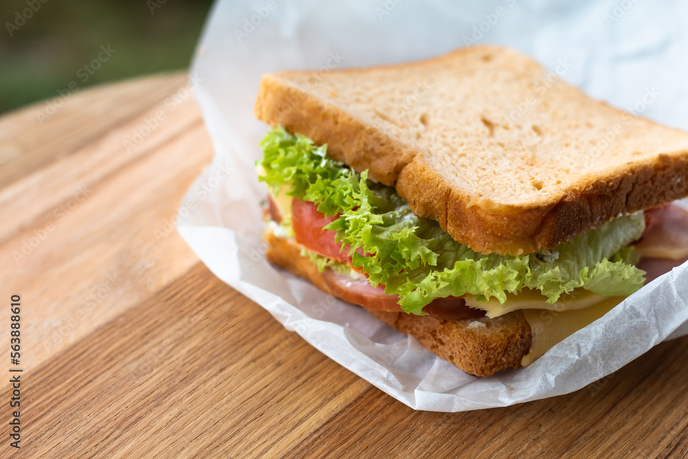 Fresh sandwich with lettuce and tomato.
Lies on a wooden plate.