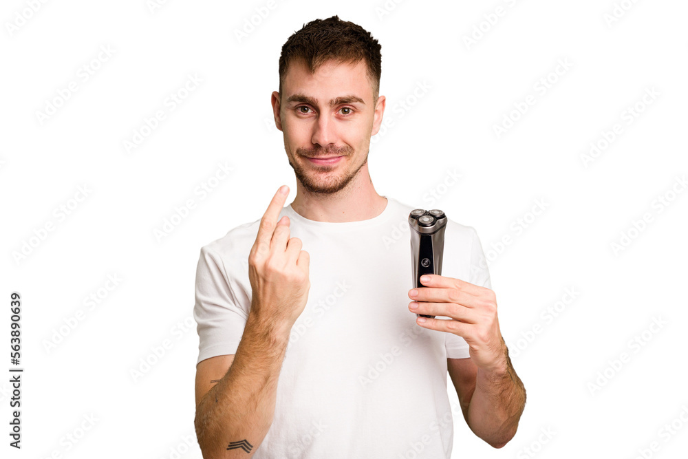 Young man holding a shaving machine cut out isolated pointing with finger at you as if inviting come closer. Young man holding a shaving machine cut out isolated pointing with finger at you as if inviting come closer.