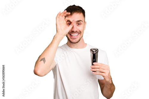 Young man holding a shaving machine cut out isolated excited keeping ok gesture on eye.
