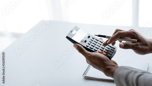 Fotografija Businessman is using a calculator to calculate company financial figures from earnings papers, a businessman sitting in his office where the company financial chart is placed