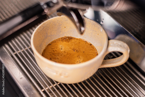 Preparing coffee with bar coffee machine, coffee is poured in a ceramic cup, close up