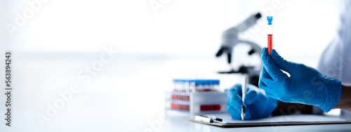 Obraz na plátně Lab assistant, a medical scientist, a chemistry researcher holds a glass tube through the blood sample, does a chemical experiment and examines a patient's blood sample