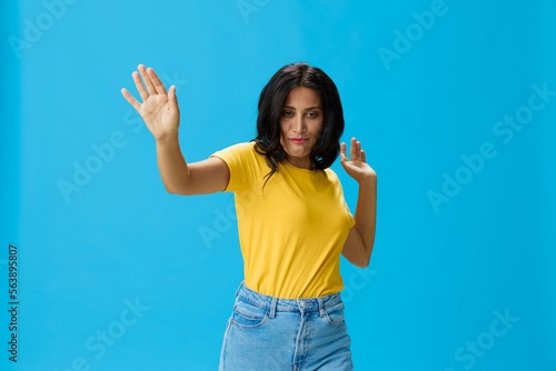 Woman in yellow t-shirt on blue background posing gestures emotions and signals with smile, hands up happiness copy space