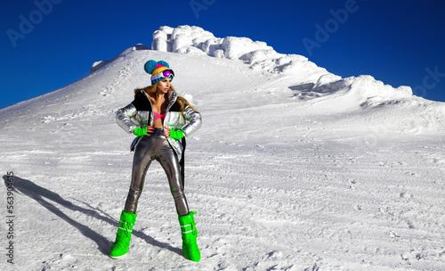 Sexy girl in silver cosmic outfit silver and winter boots is posing in the mountains. Female model in glamour silver jumpsuit in winter scenery. photo