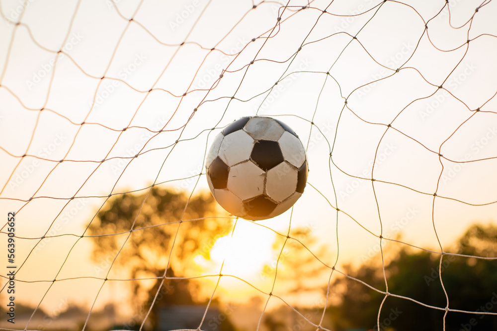 Naklejka premium A ball in goal net for street soccer football under the sunset ray light. Film picture style.