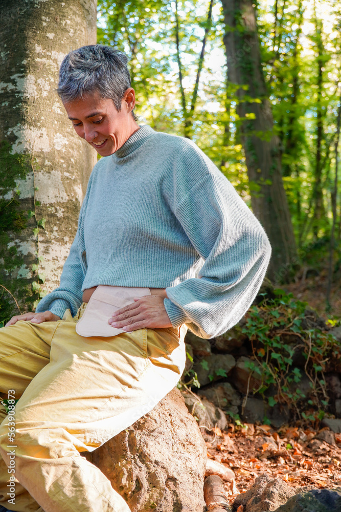 Fototapeta premium woman looking at ostomy bag after colon cancer in the forest
